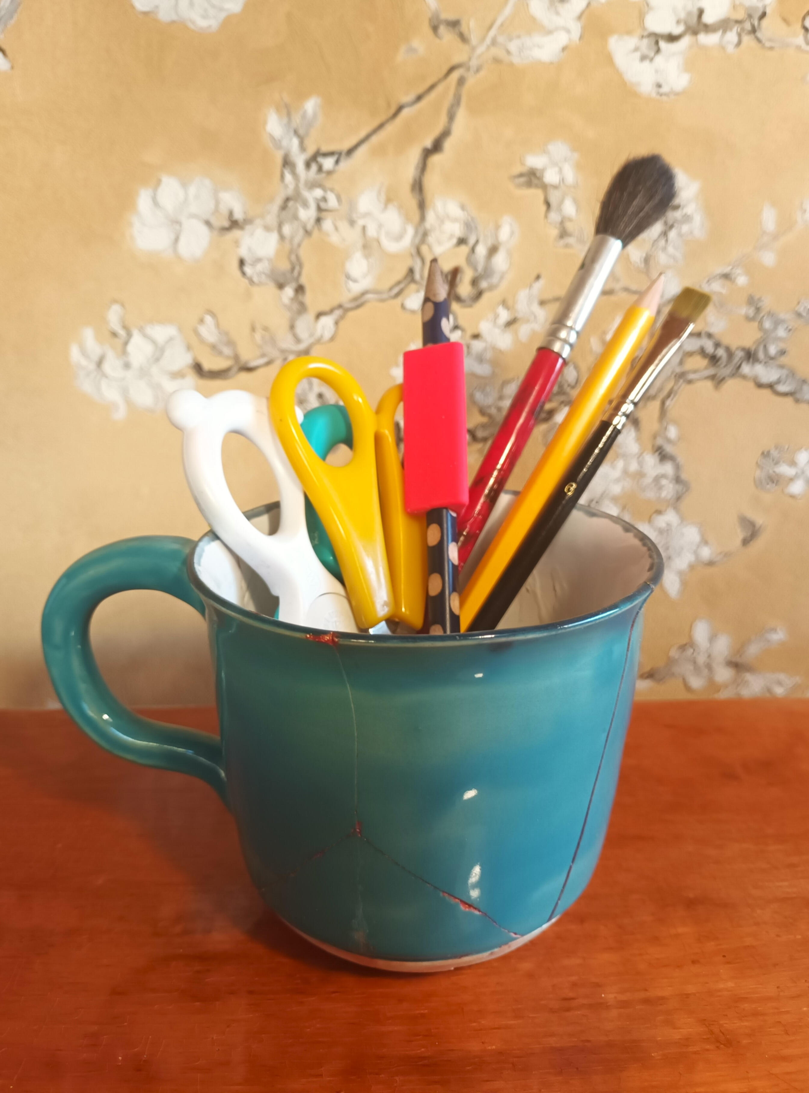 Kuvituskuva: Kyniä ja siveltimiä turkoosissa kupissa.