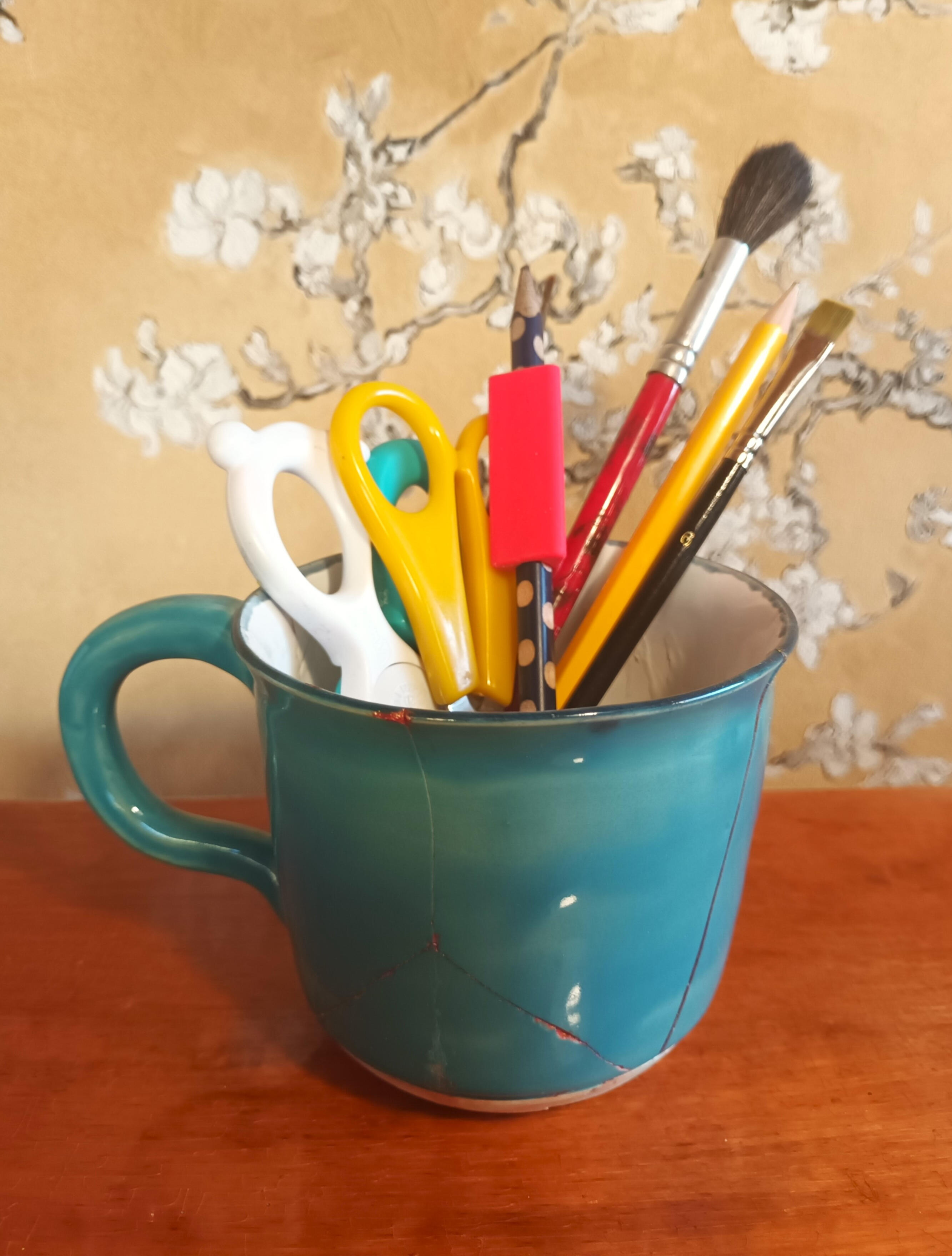 Kuvituskuva: Kyniä ja siveltimiä turkoosissa kupissa.